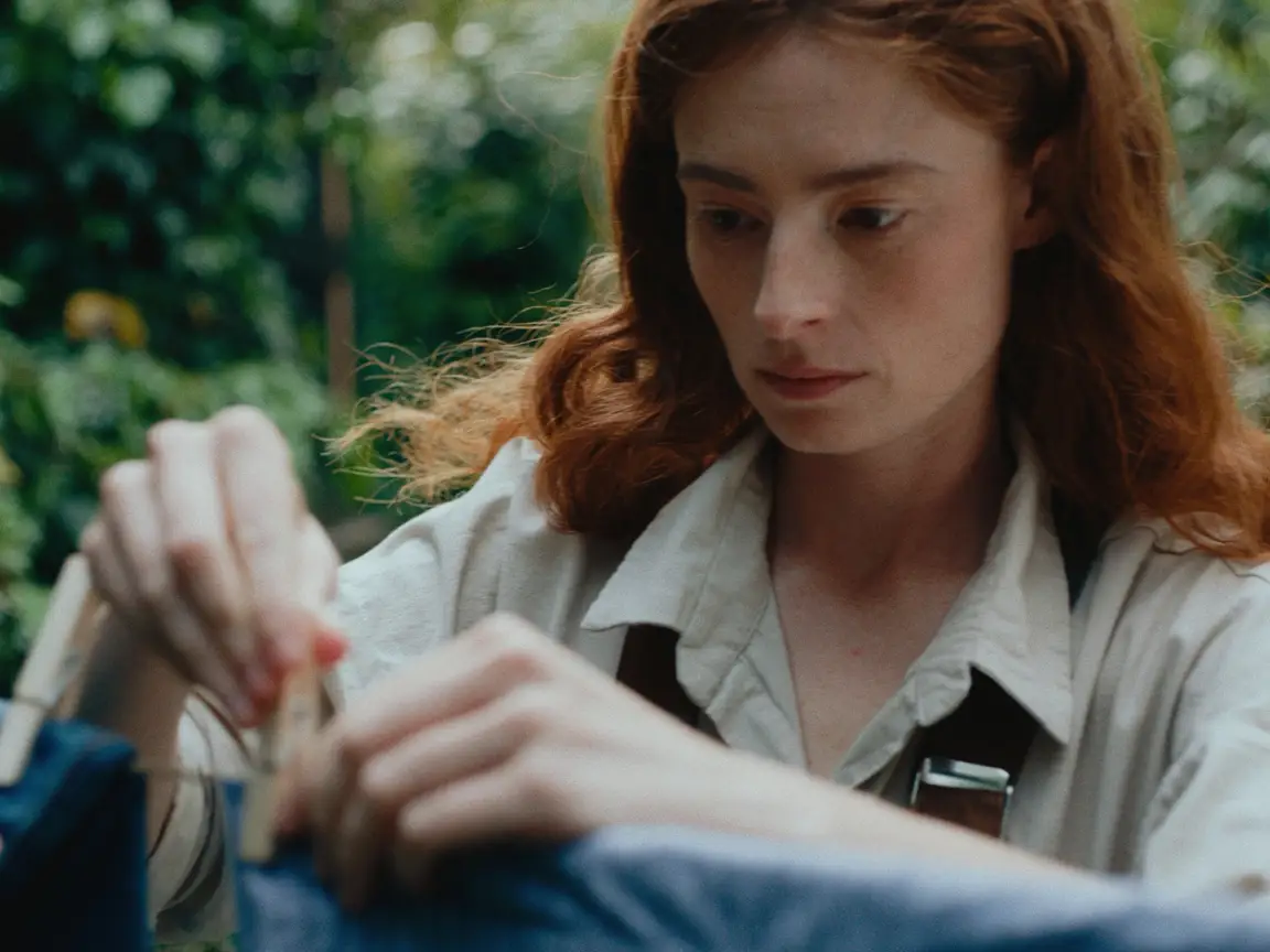 Moonlight Woman: a red haired woman pins laundry to a clothesline in a leafy green garden