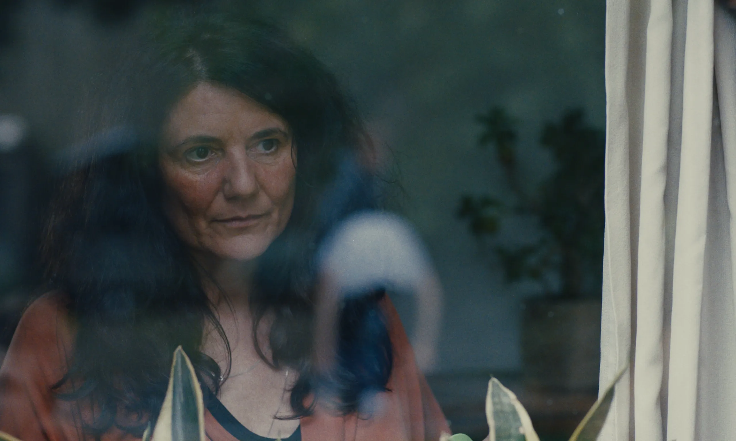 Today We Escape: a dark-haired woman watches through window glass streaked with reflections