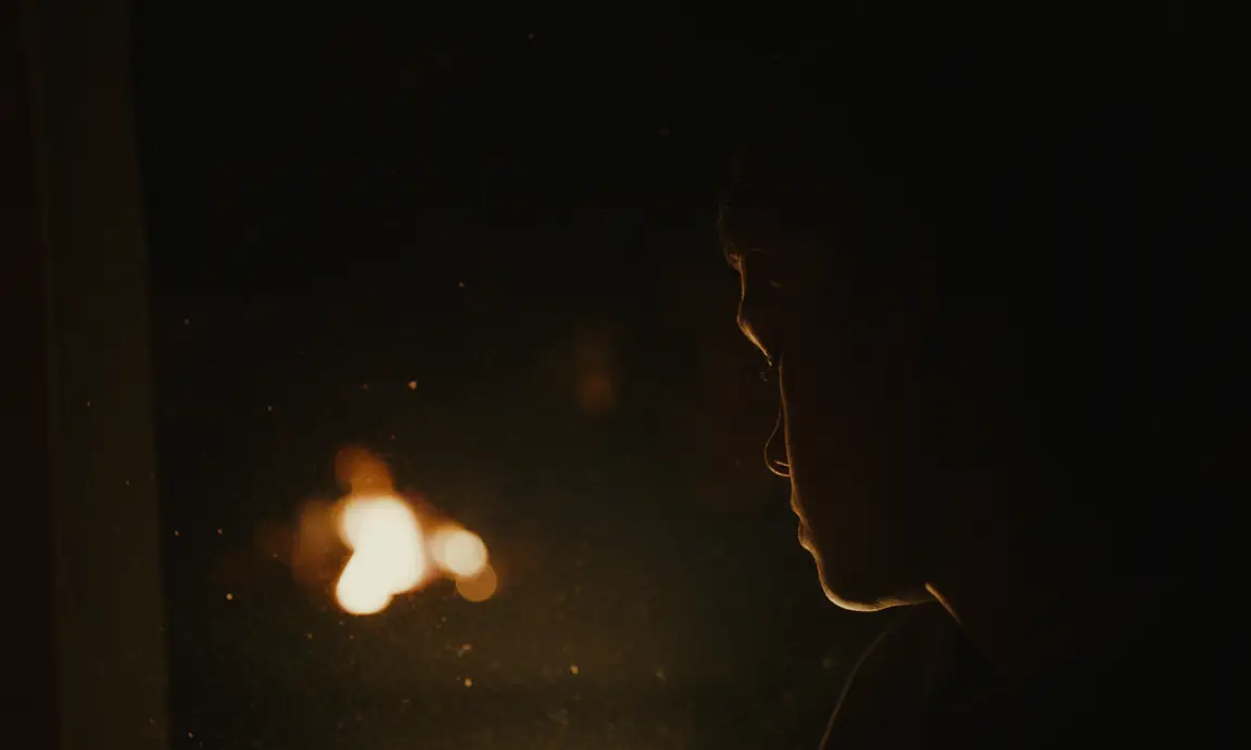 Today We Escape: rim-lit profile of a boy in darkness beside a blurred flame
