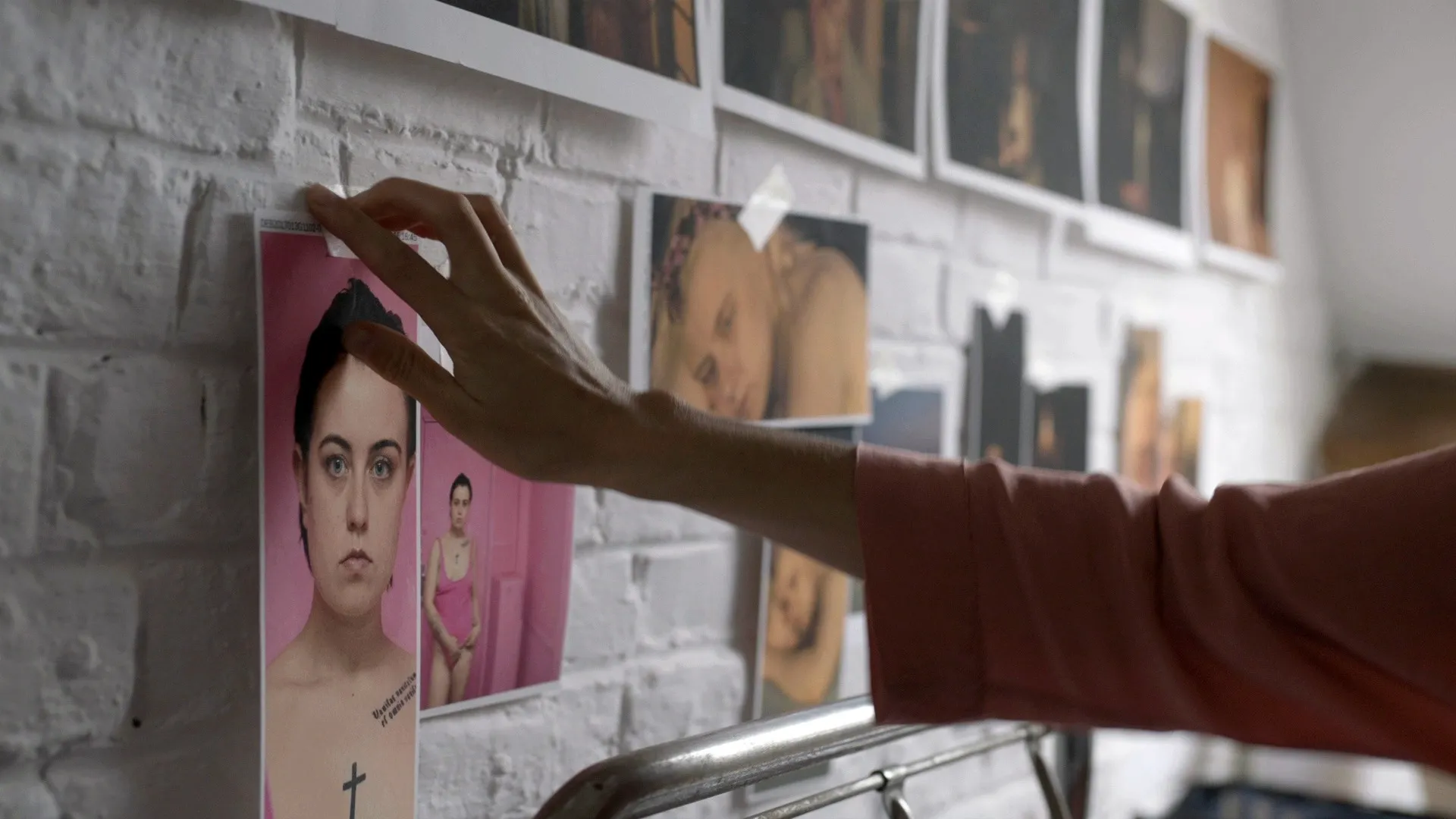 Chance Encounters: a hand pinning portraits to a white brick wall covered with taped photographs