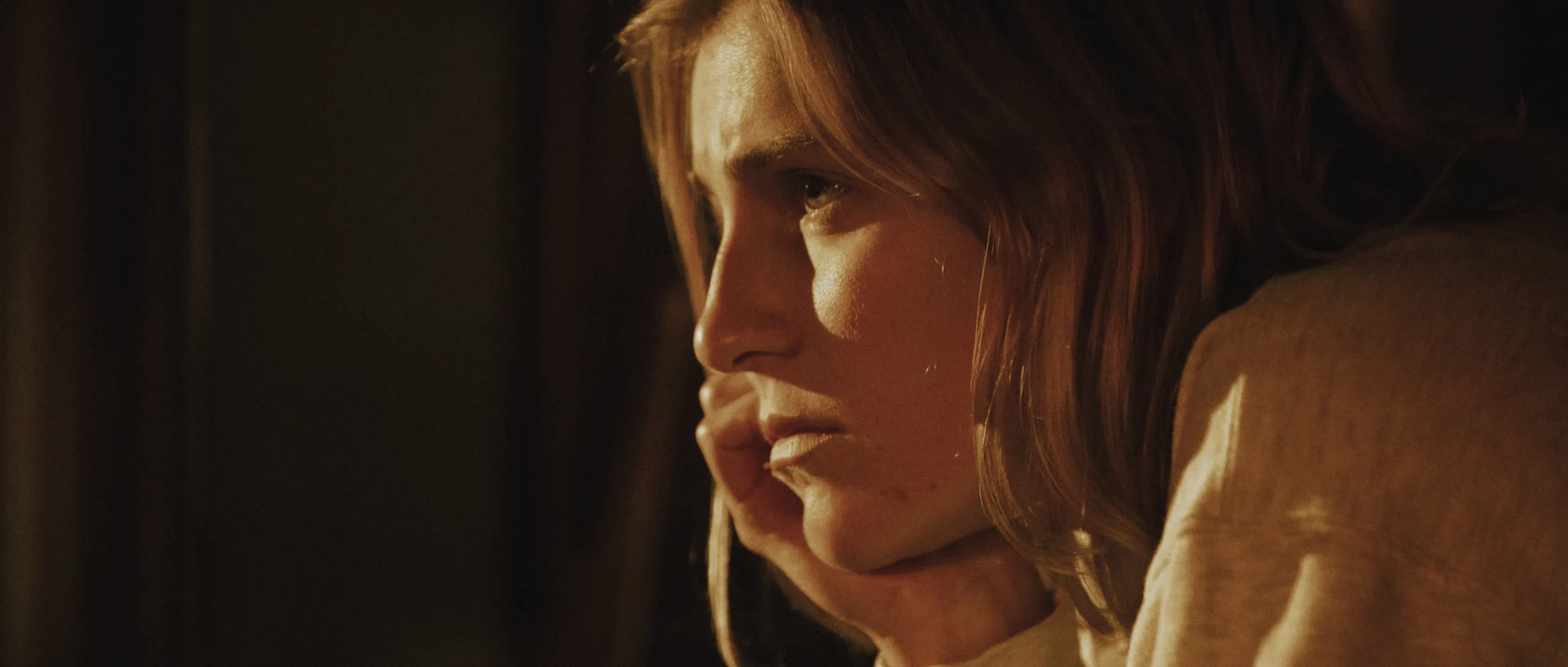 Anna: profile close-up of a woman with a tense, worried expression in warm dim light