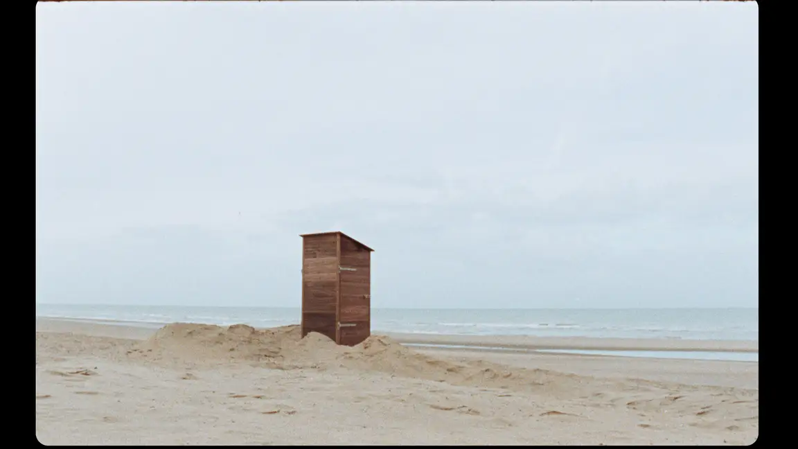 Hoge Blekker: lone wooden beach cabin half-buried in a sand mound, facing the flat grey sea and horizon