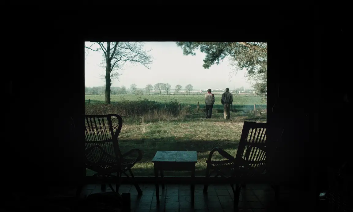 Felix, Le Gamin Qui Traverse: two men walk away across a misty field seen through a dark window past empty chairs