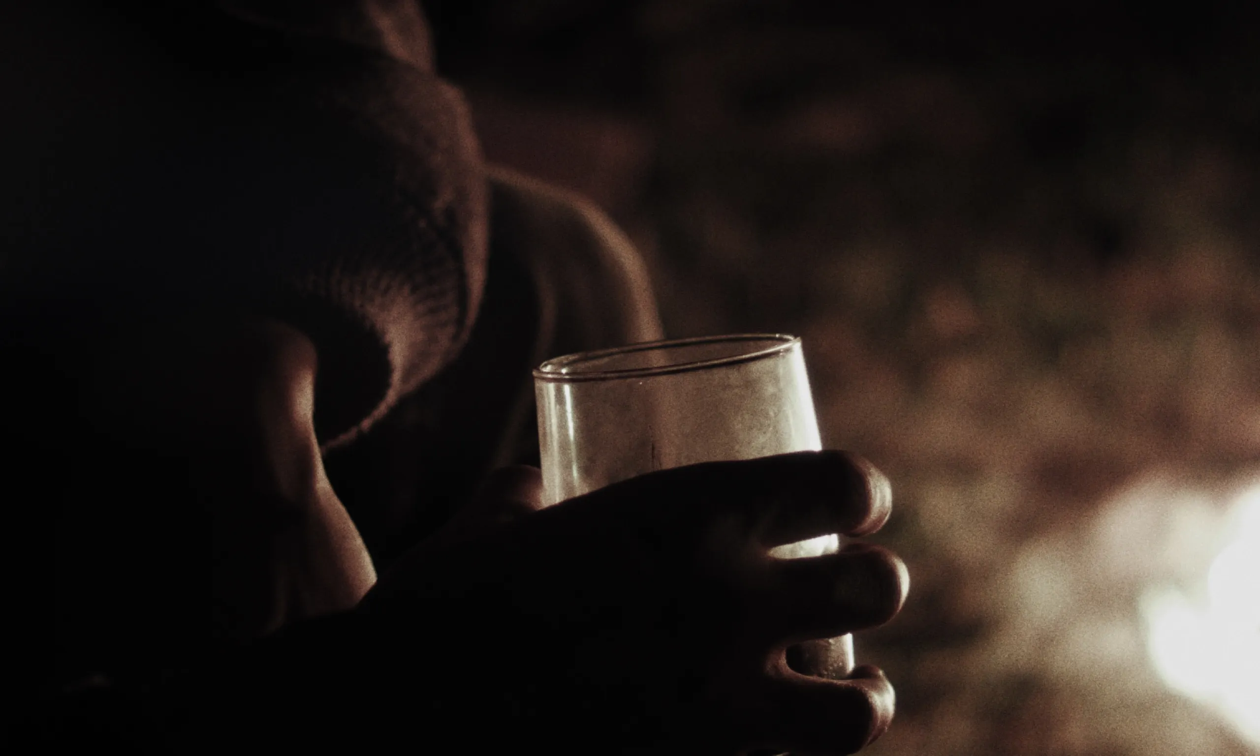 Felix, Le Gamin Qui Traverse: hands cradle an empty drinking glass in warm firelight against a dark background