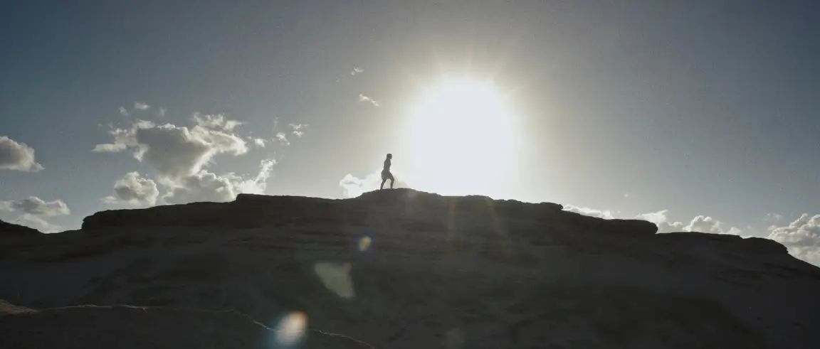 Springtide: a silhouetted figure walks along a rocky ridge crest against the glaring sun