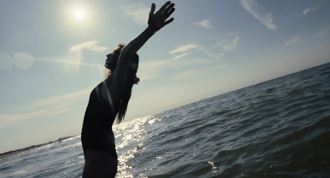 Burn: a woman in a swimsuit stretches her arms toward the sun above a glittering sea