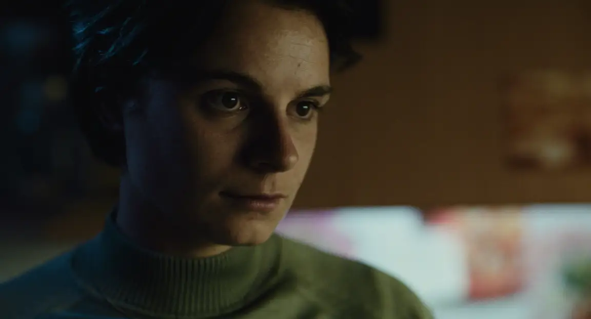 Burn: close-up of a pensive woman in a green turtleneck in a dark warm-lit room