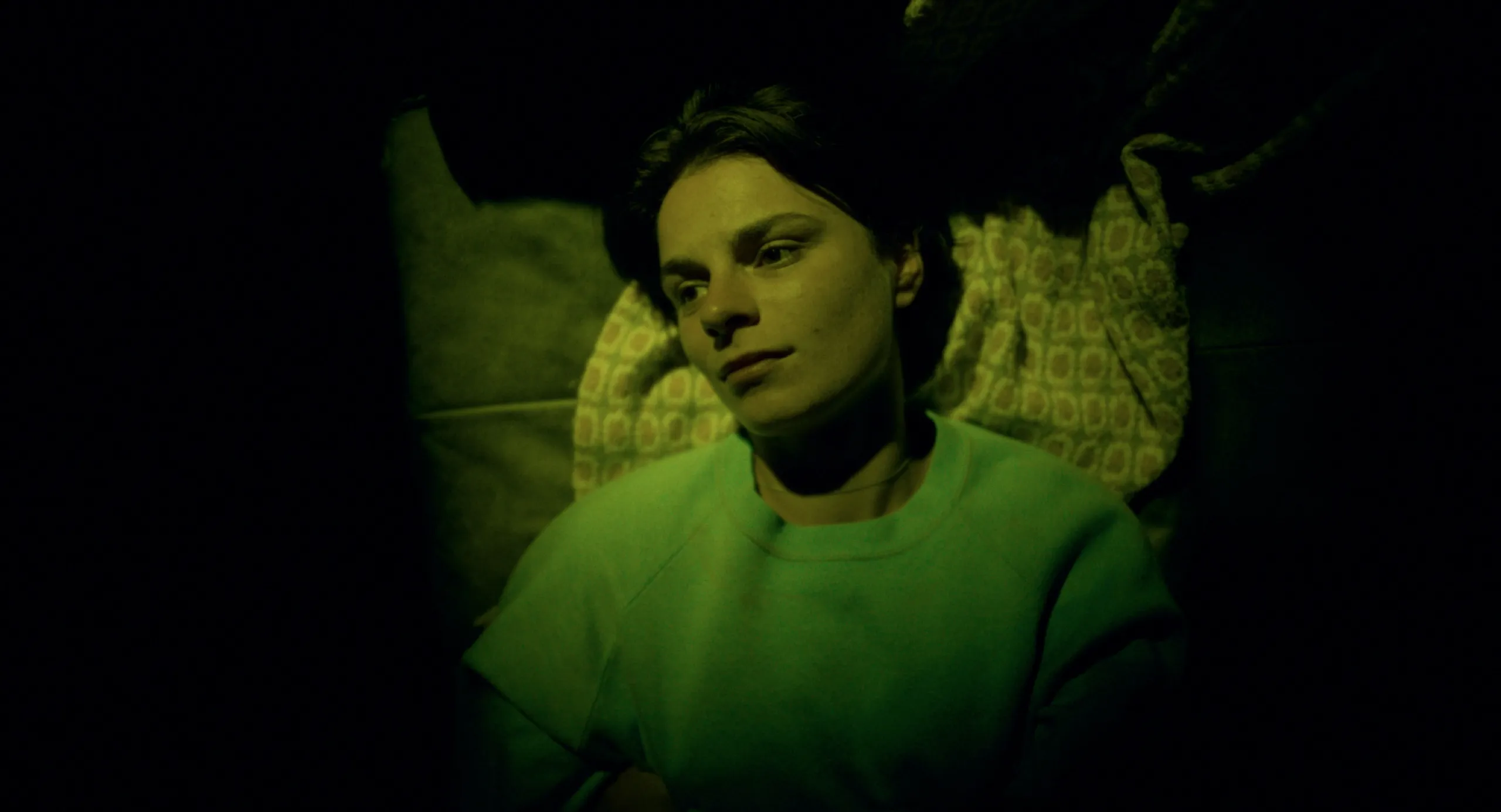 Burn: a woman in a green sweater lies awake against patterned pillows in dim green light