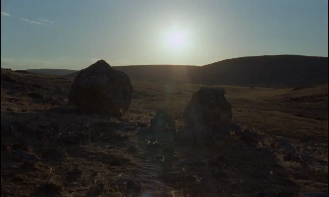 Ever Since, I Have Been Flying: two large boulders on a golden dry hillside as the sun sets behind