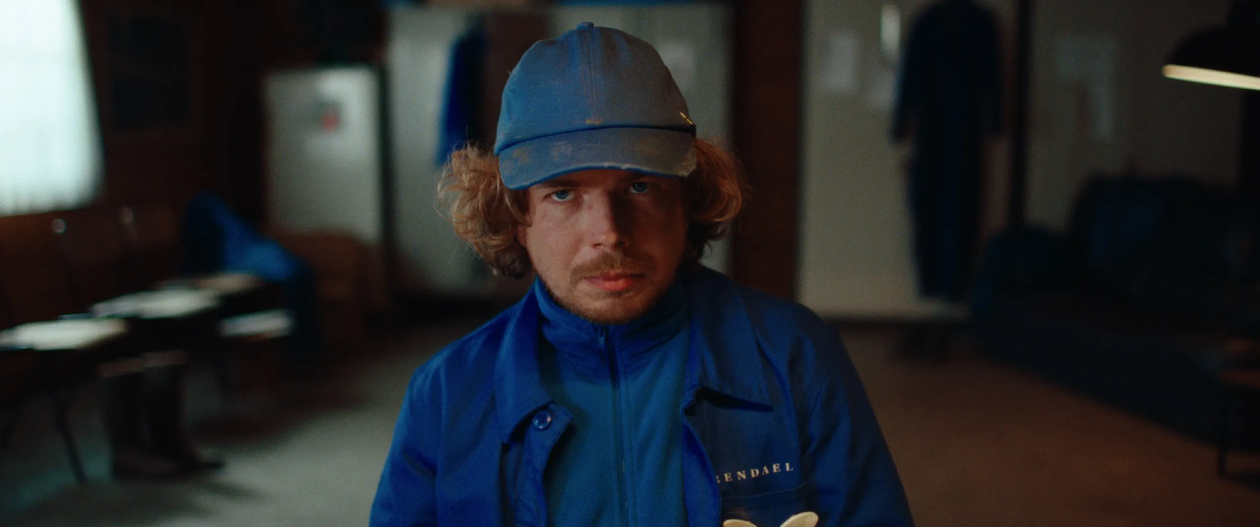 Vlinderman: Joop in blue cap and uniform stares straight ahead in a dim staff room