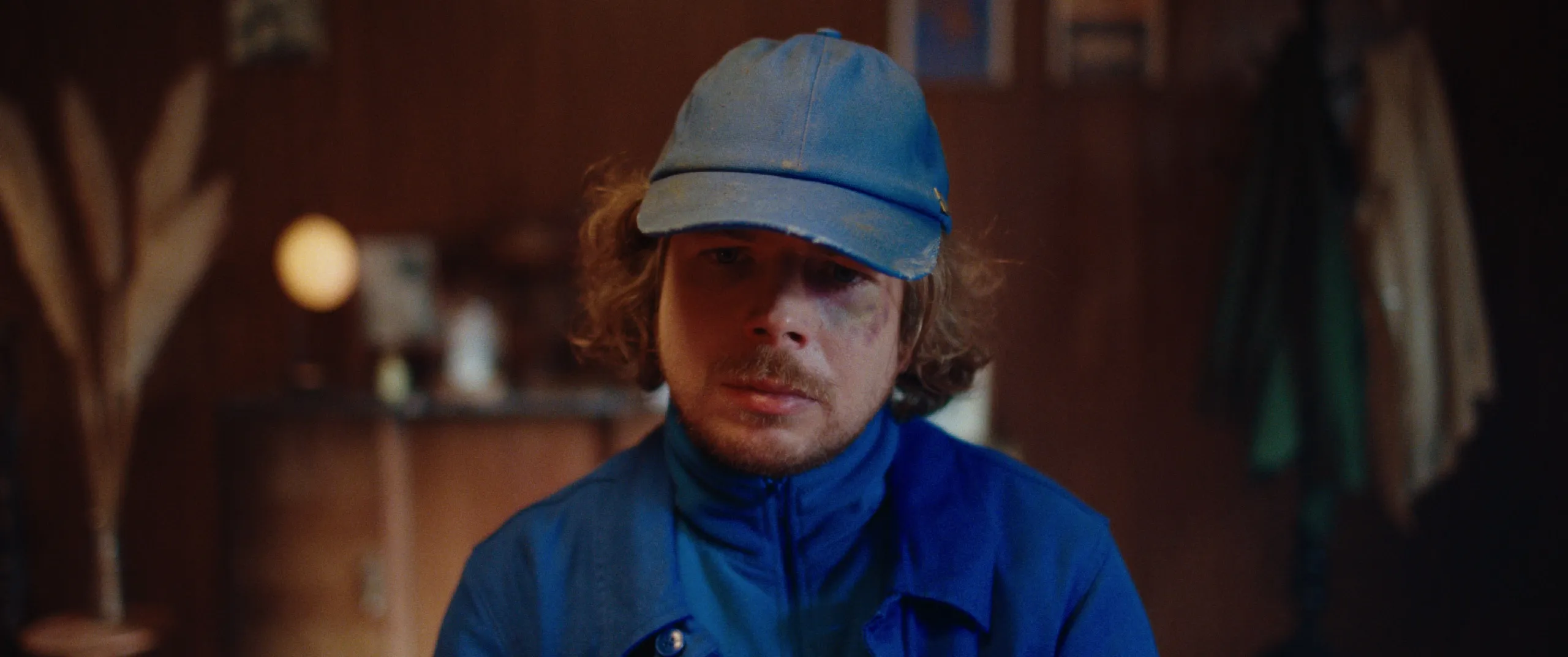 Vlinderman: Joop faces the camera with a bruised eye in a warm wooden room