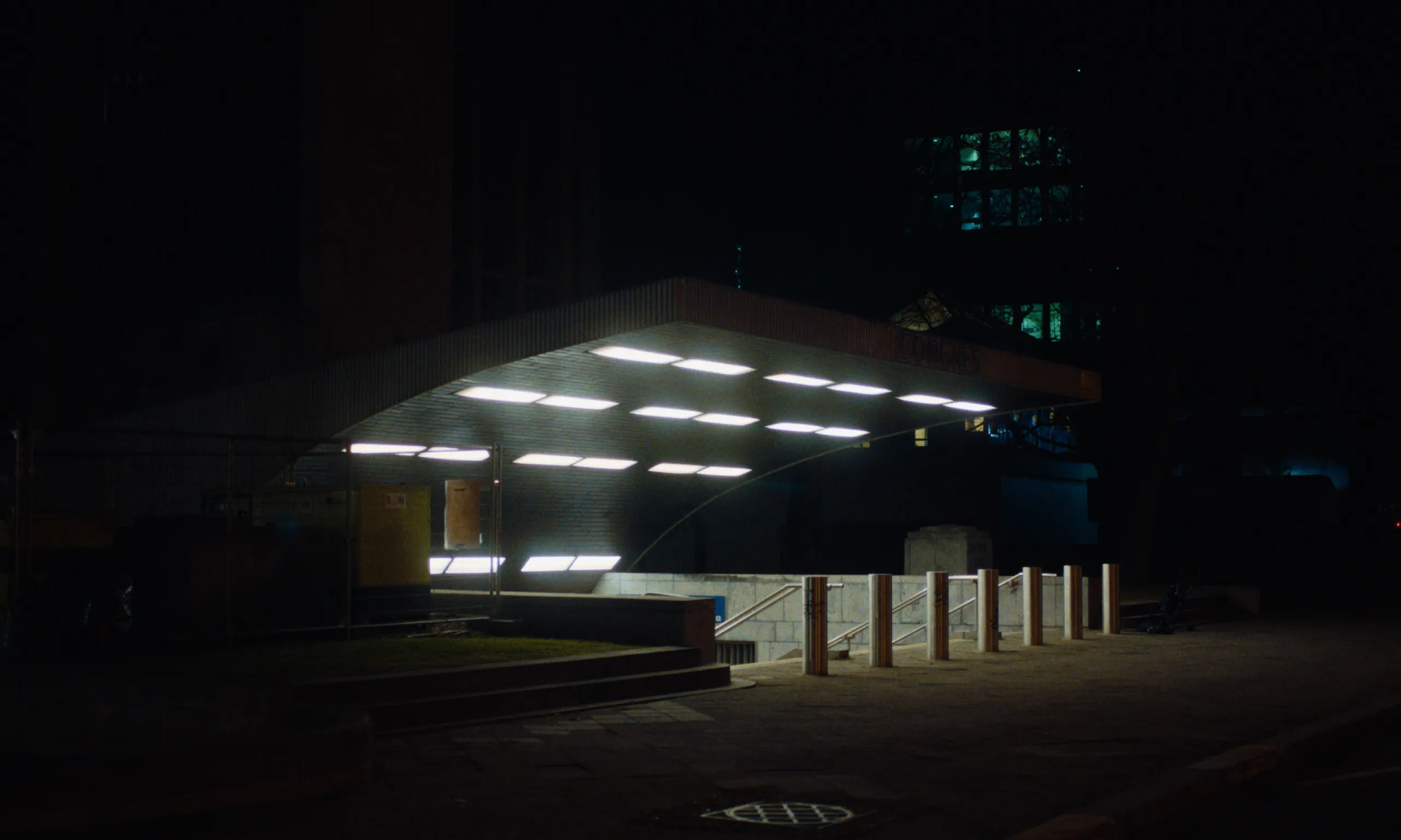Burning Clouds: fluorescent panels glow under the curved canopy of a metro entrance at night