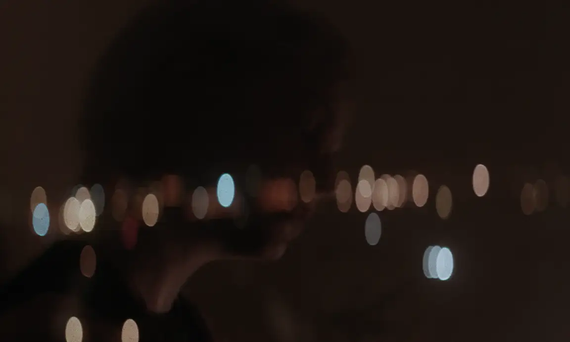Les Homards Immortels: dark profile of a woman at night against blurred city lights in warm bokeh