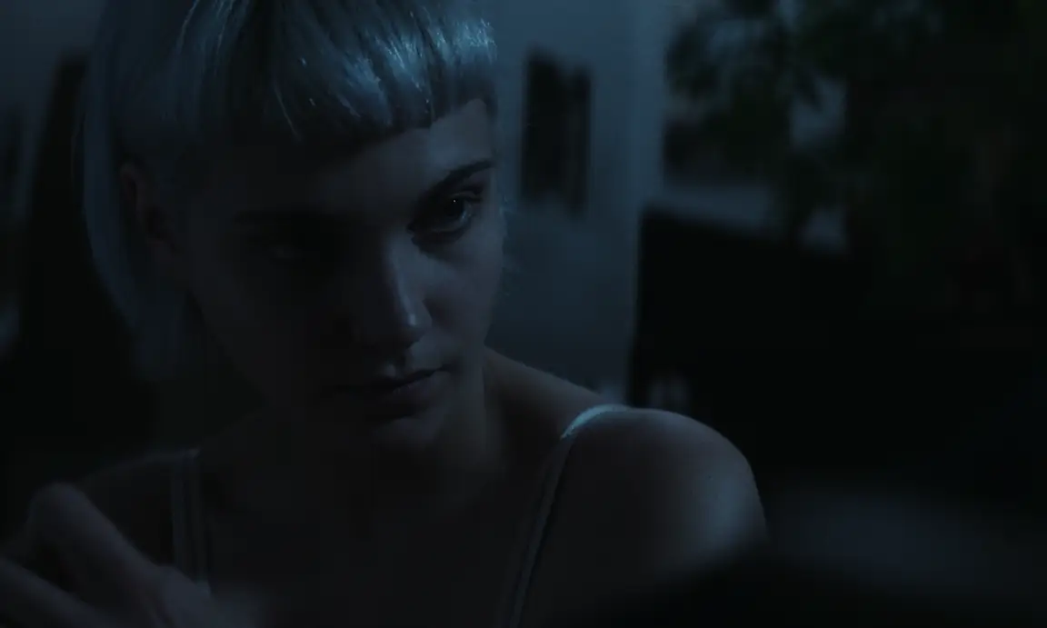 Les Homards Immortels: young woman with a white blonde fringe glances aside in a dim blue room