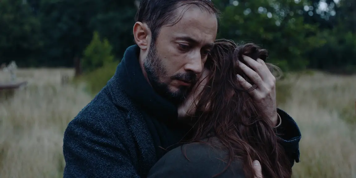 The Tears of Things: a bearded man holds a woman close in a tender embrace in a field
