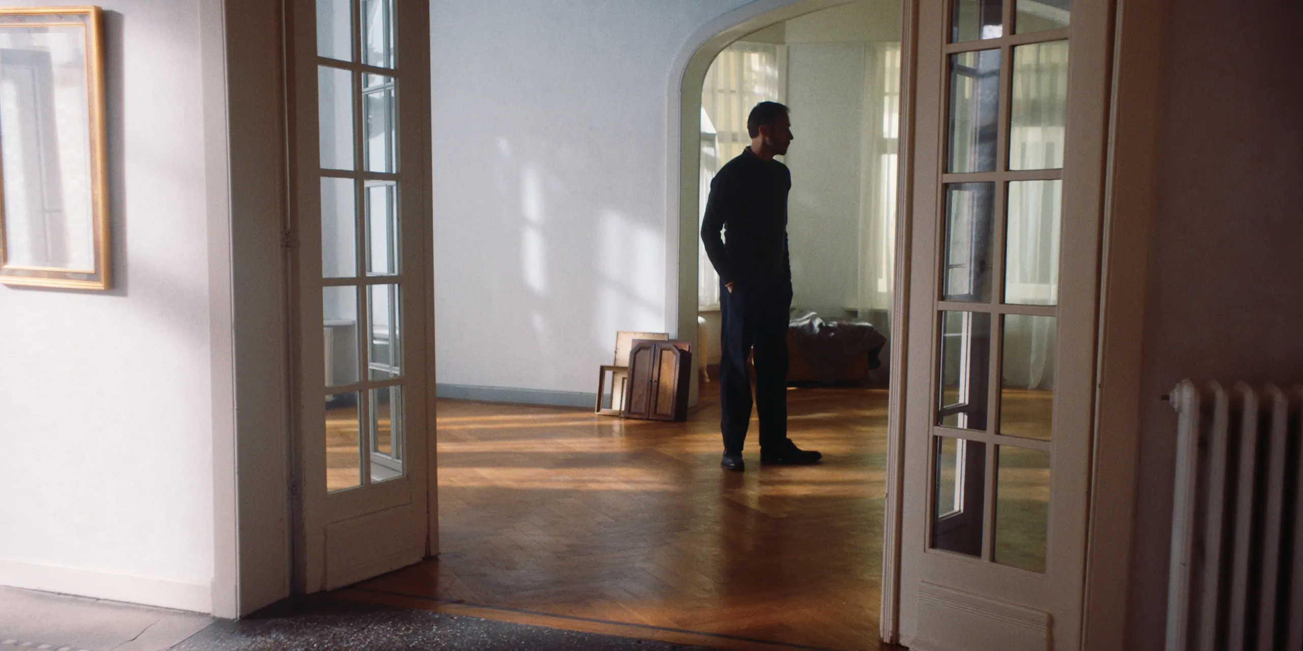 The Tears of Things: a man stands alone in a bright empty apartment seen through open glass doors