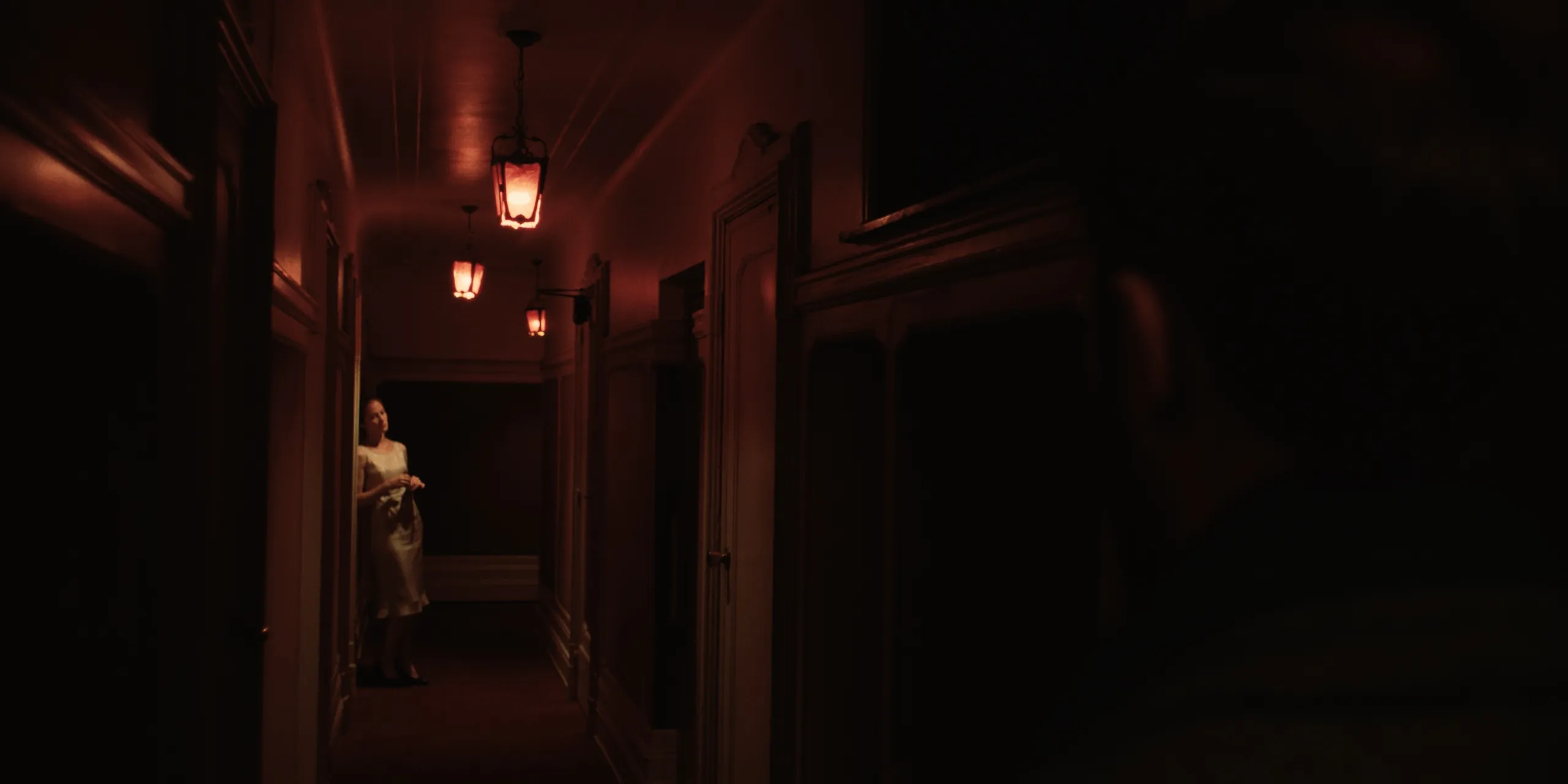 The Tears of Things: a woman in a slip stands in a dim hallway under warm red hanging lanterns