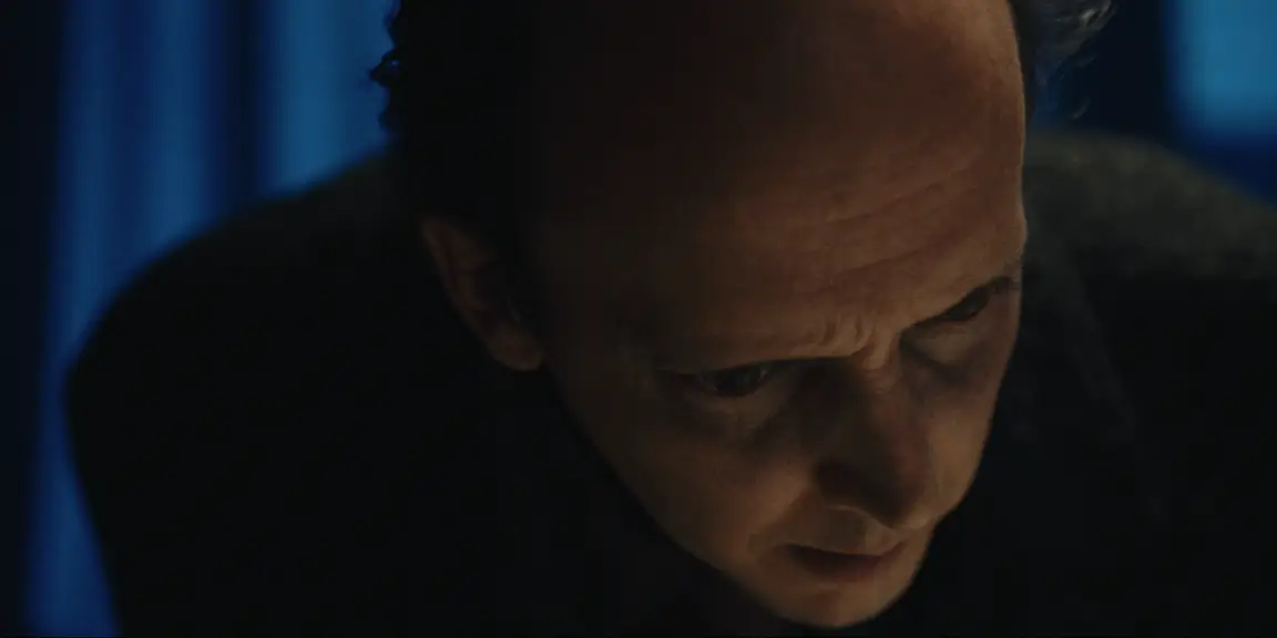 Bearer of Bad News: Sven bows his head in thought, forehead furrowed, blue curtains softly lit behind