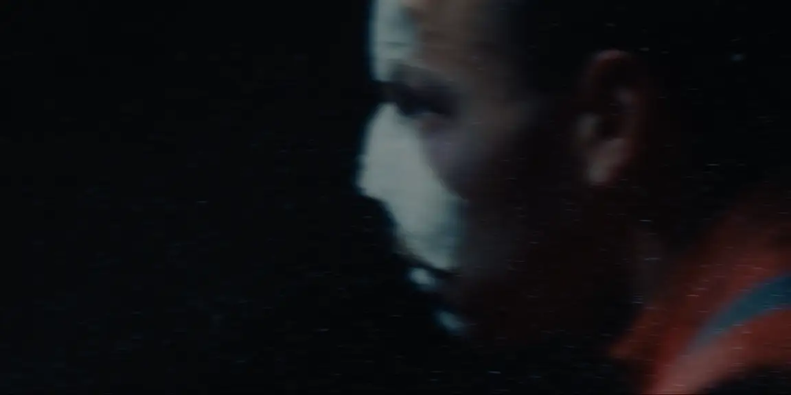 Bearer of Bad News: blurred profile of the bandaged worker in an orange jacket moving through darkness
